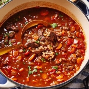 Beef barley vegetable soup in a Dutch oven with a ladle full of soup.