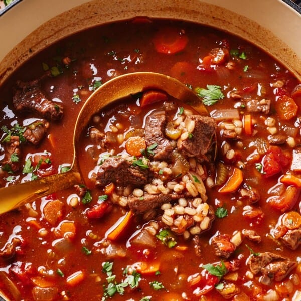 Beef barley soup in a Dutch oven with a ladle full of soup.