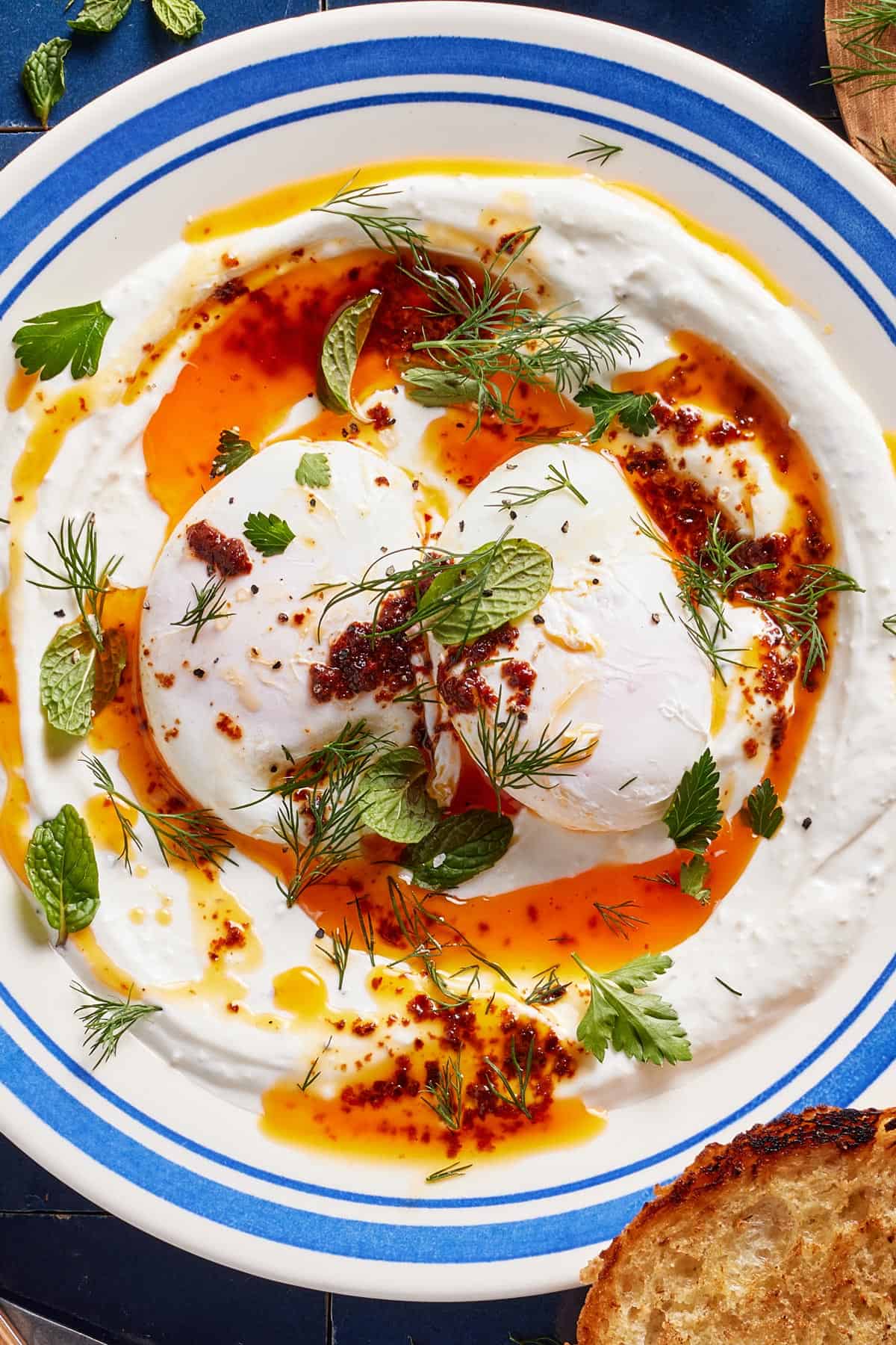 Turkish eggs placed on a plate with yogurt and spicy butter sauce and garnished with herbs.