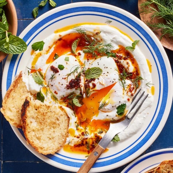 Turkish eggs (aka cilbir) on a plate from the top view with two slices of bread on the side.