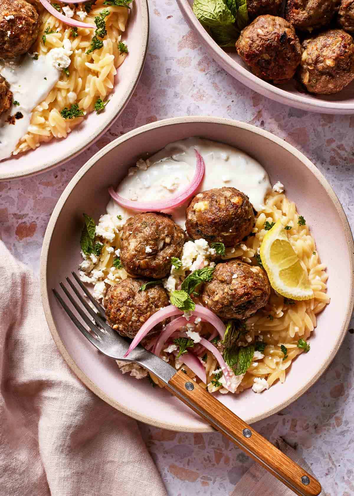 Greek lamb meatballs served over a bed of lemon orzo garnished with tzatziki sauce and mint.