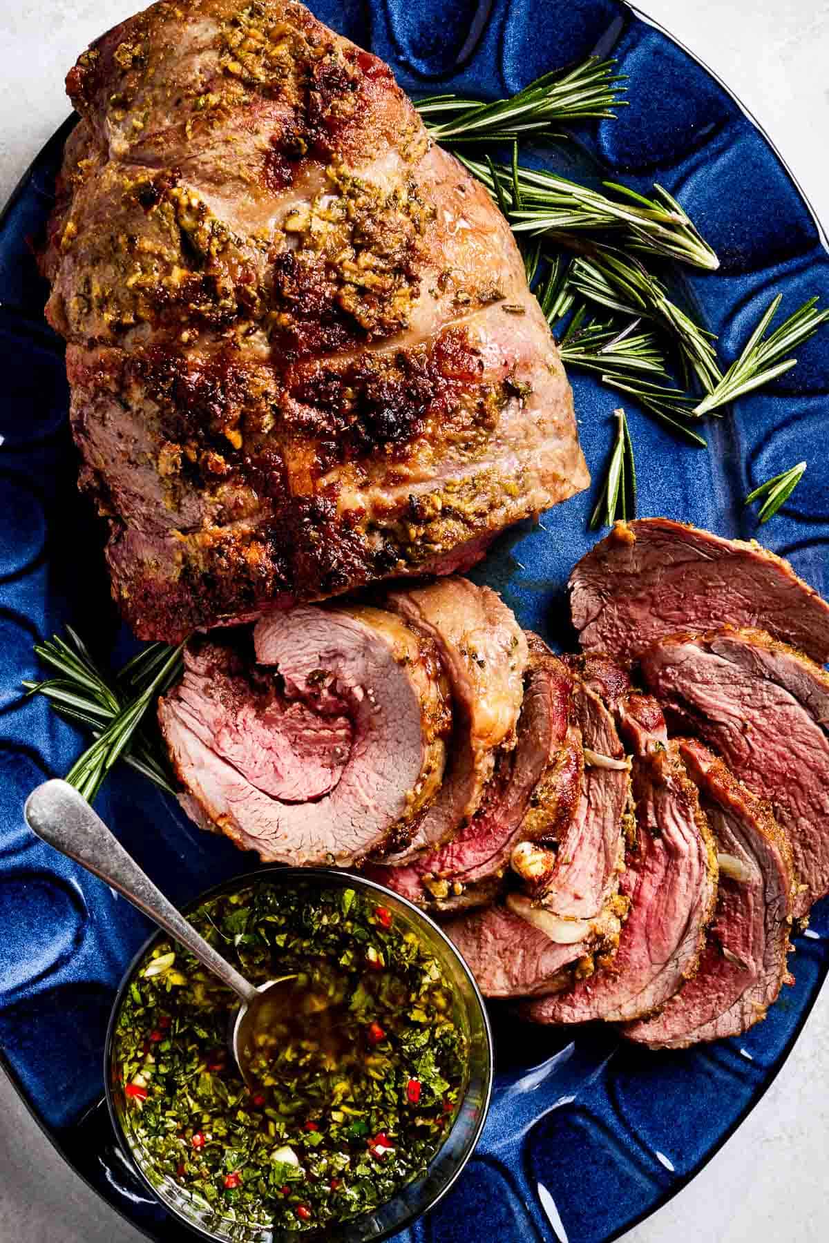 Boneless leg of lamb roast sliced and served with mint sauce on the side.