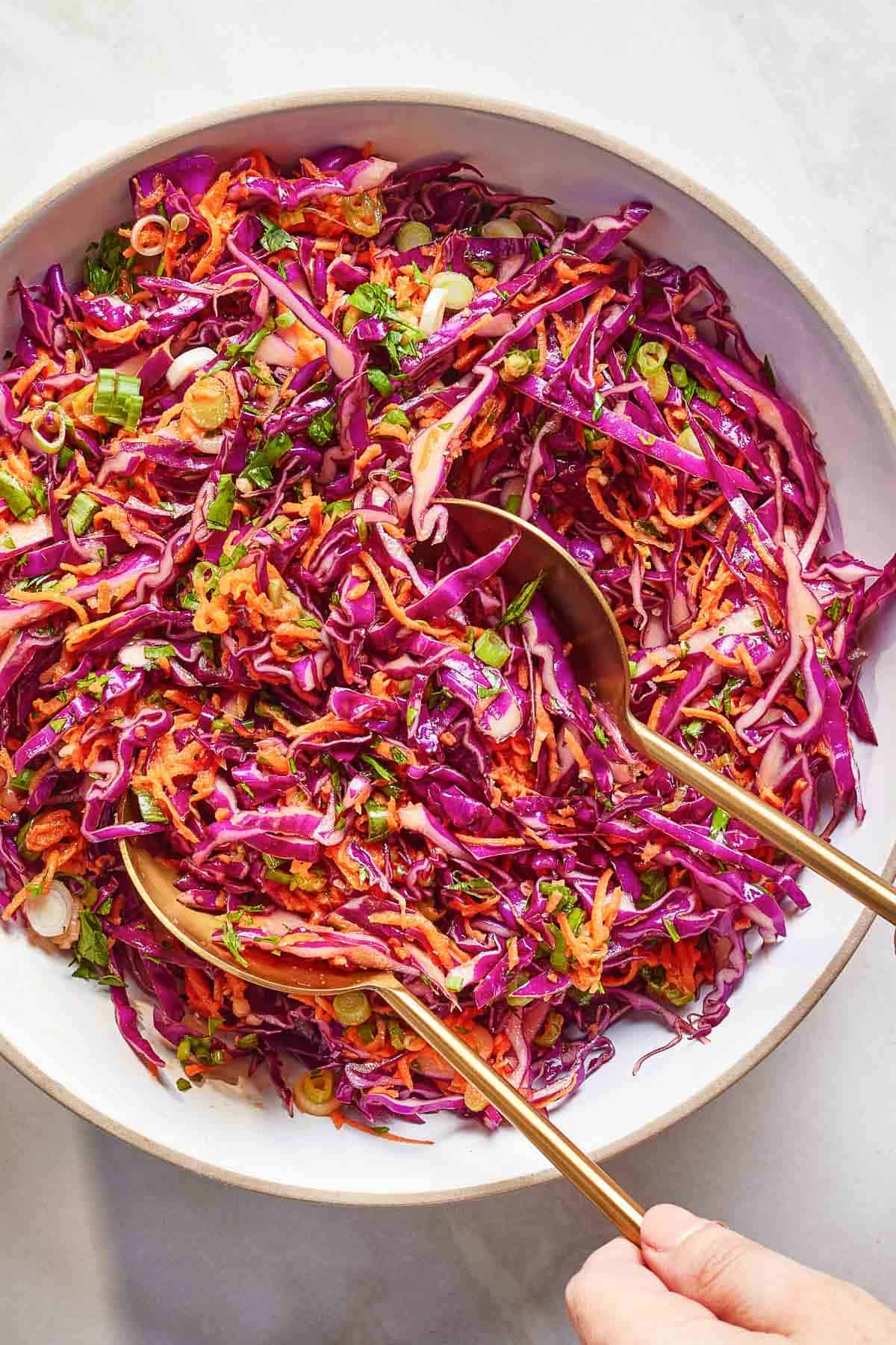 Red cabbage coleslaw in a bowl with utensils from the top view.