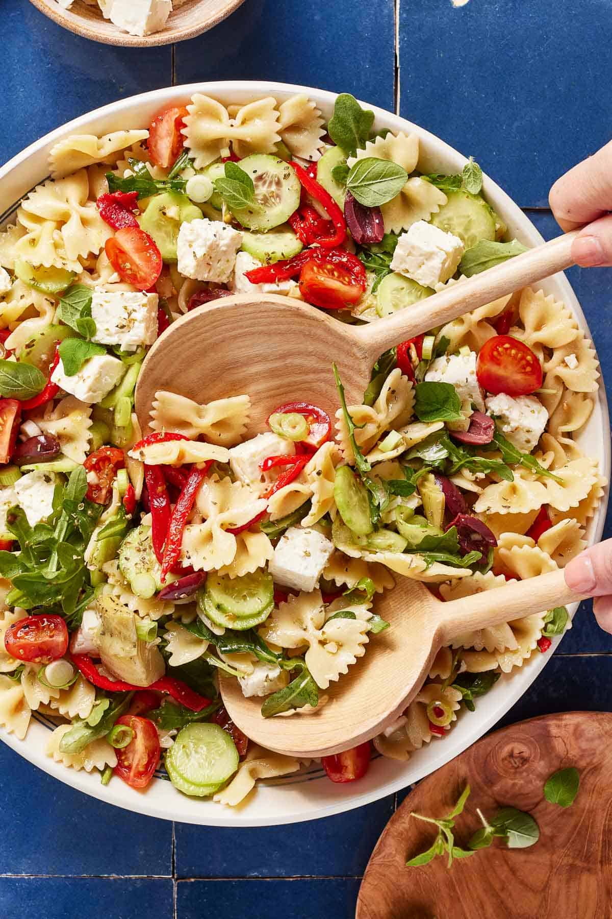 Cold Mediterranean pasta salad in a bowl with wooden spoons from the top view.