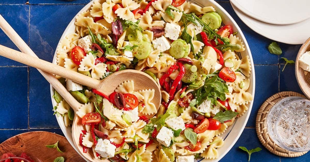 A Mediterranean pasta bowl with wooden spoons inside the bowl.