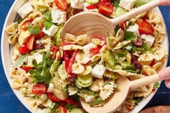 Pasta salad in a bowl with wooden utensils.