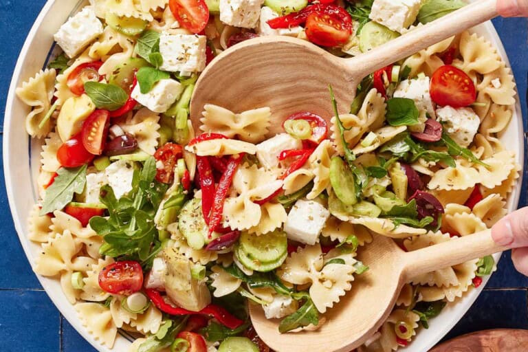Pasta salad in a bowl with wooden utensils.