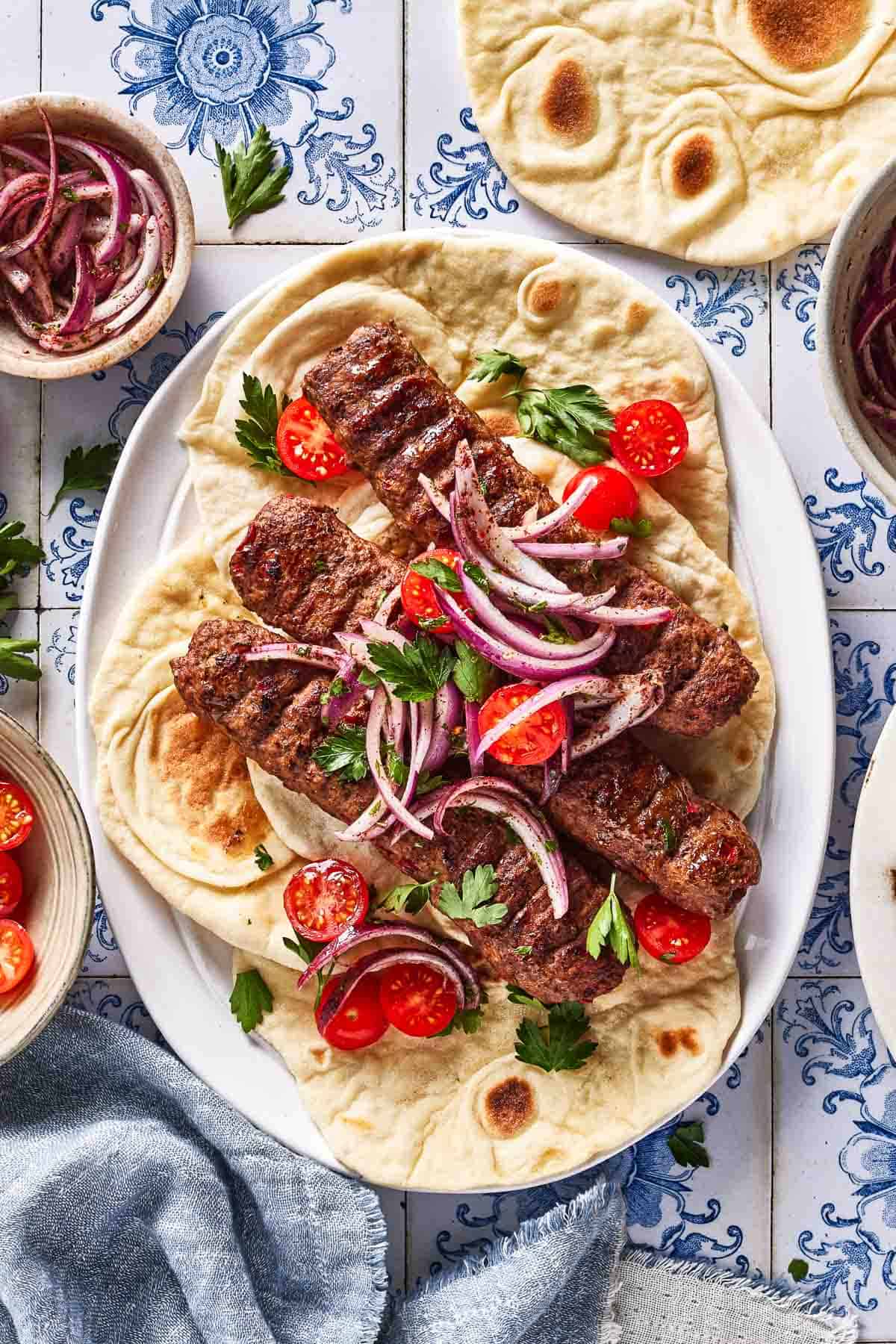 Adana kebab garnished with sumac onions and tomatoes on a plate.