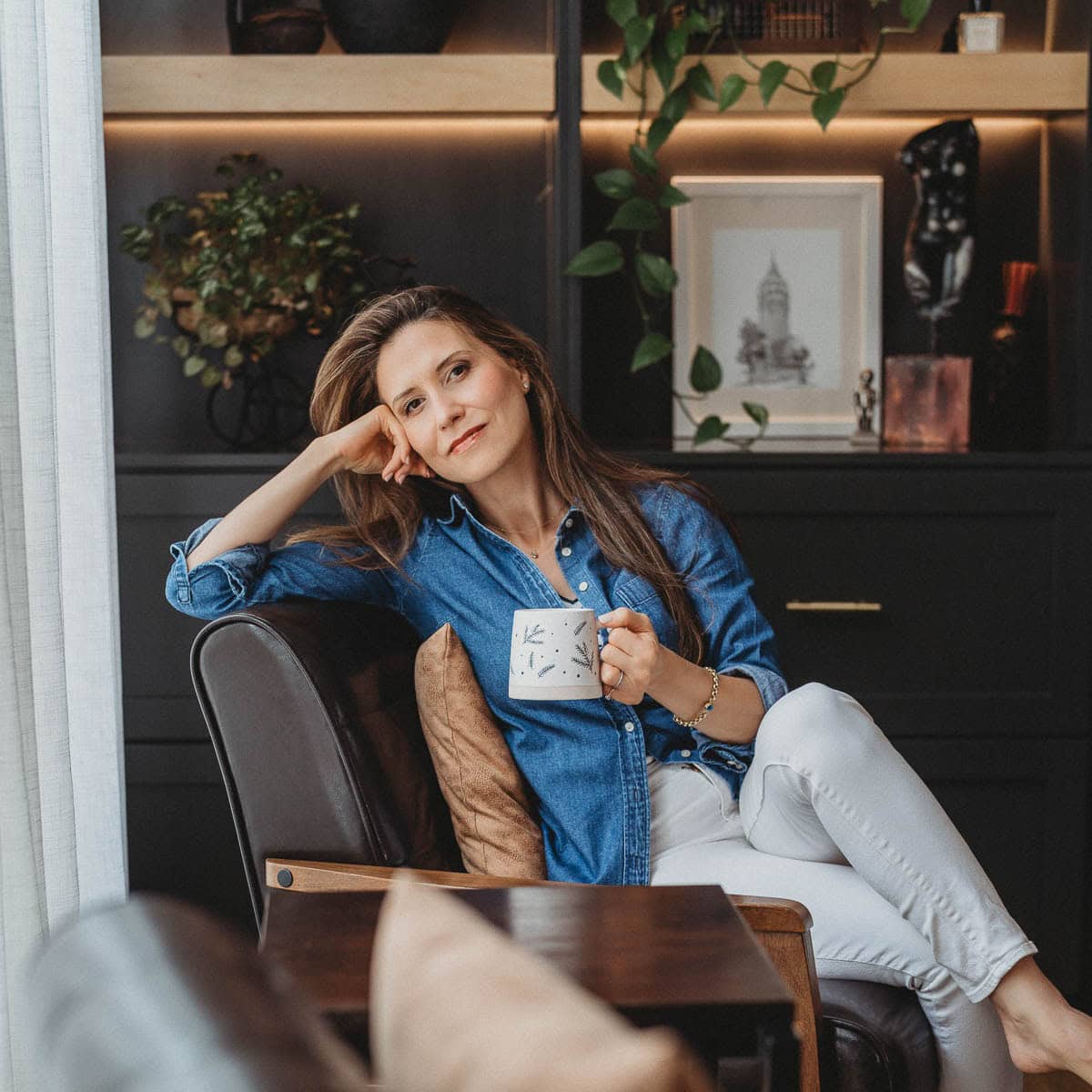 Aysegul Sanford sitting in a chair with a coffee cup in her hand.