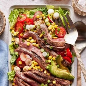 Grilled flank steak salad with utensils on the side.