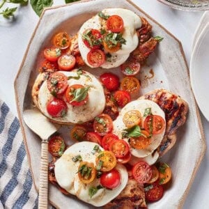 Grilled Caprese chicken garnished with tomato salad and basil.