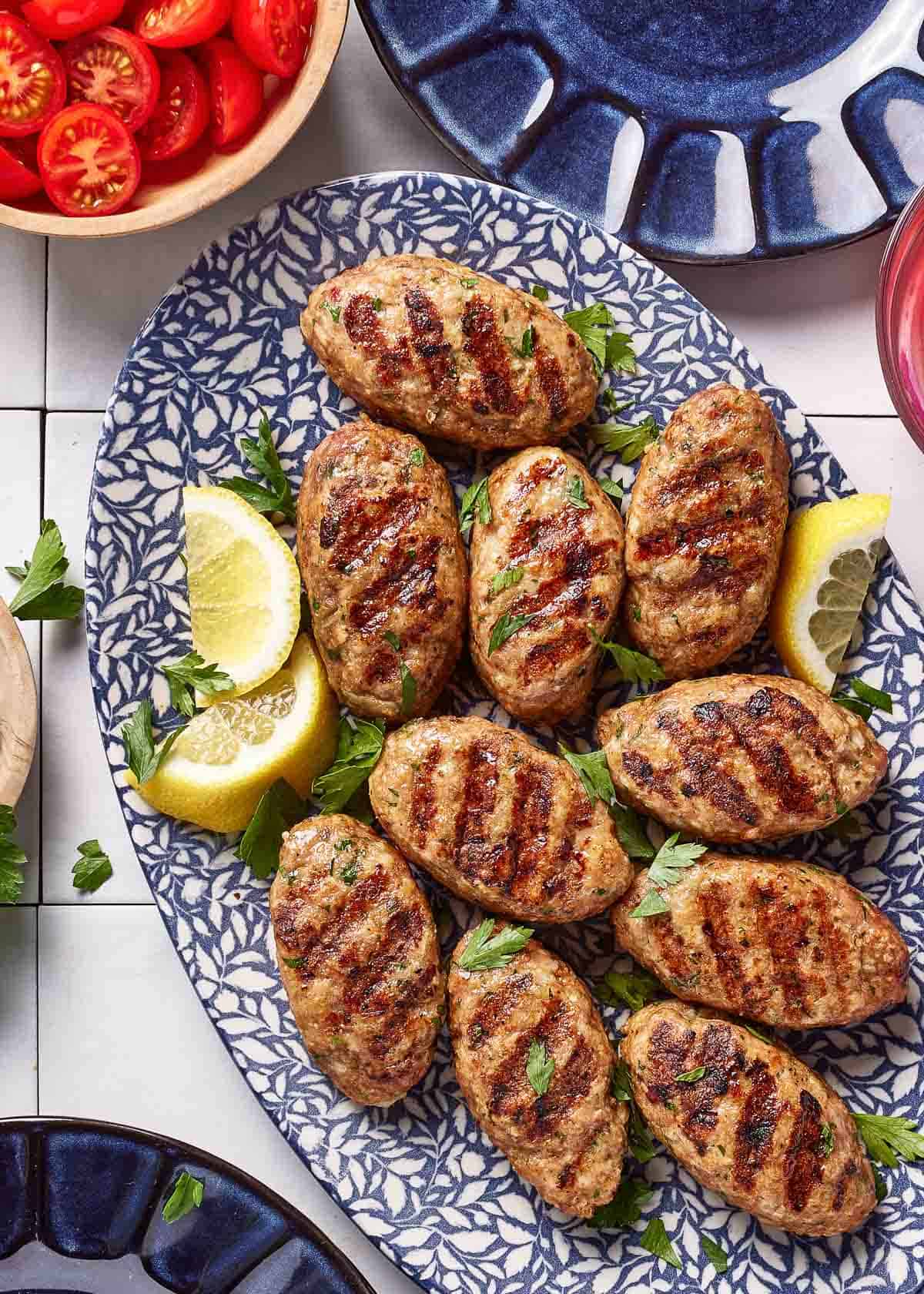Grilled chicken koftas on a plate served with lemon wedges.