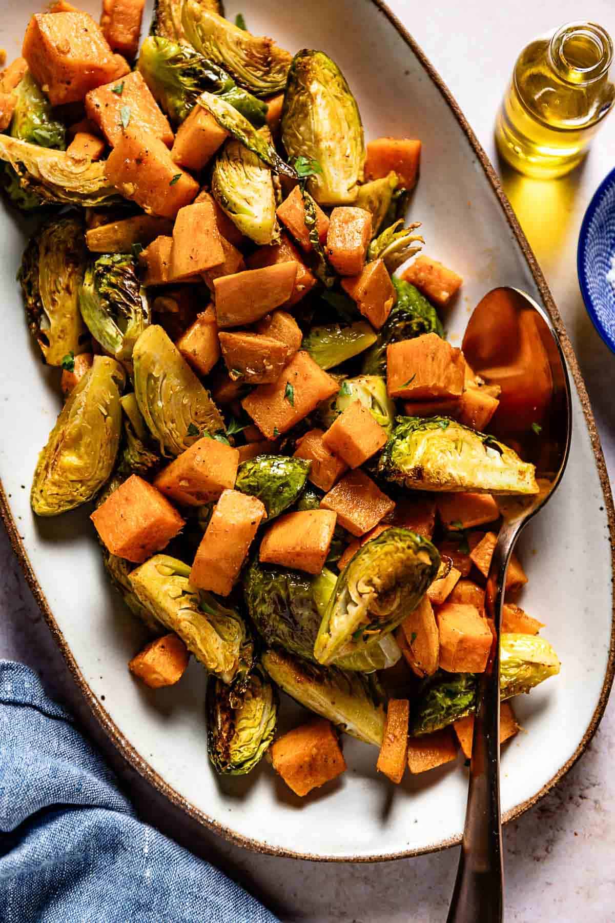 Roasted sweet potatoes and brussels sprouts in a plate with a spoon on the side.