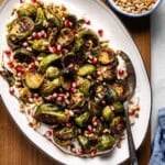 Roasted Brussels sprouts garnished with pomegranate seeds and served over yogurt tahini sauce.