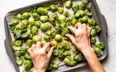 Person arranging Brussels sprouts on a sheet pan.