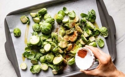 Person seasoning Brussels sprouts on a sheet pan.