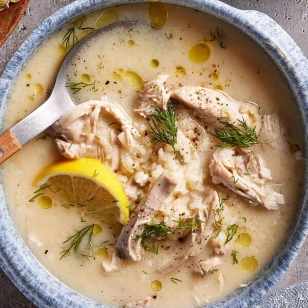 A bowl of Greek Avgolemono soup garnished with dill with a spoon in the bowl from the top view.