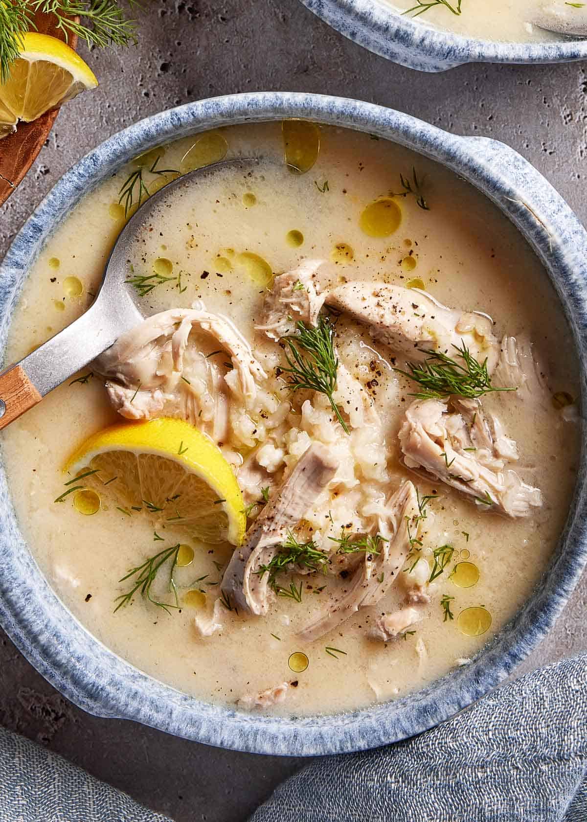A bowl of Greek Avgolemono soup garnished with dill with a spoon in the bowl from the top view.