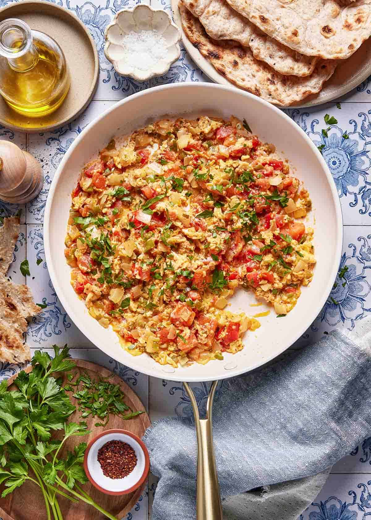 A finished skillet of traditional Menemen (Turkish scrambled eggs) with green peppers and tomatoes, served family-style with toasted bread on the side.