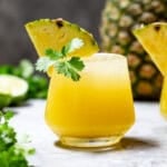 Pineapple mezcalita in a glass garnished with a pineapple wedge and fresh cilantro.