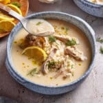 A bowl of avgolemono soup garnished with lemon and fresh dill.