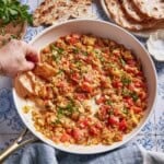 Person scooping menemen from the skillet with some crusty bread.