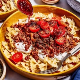 Bow tie pasta topped with spiced ground meat, creamy yogurt, and chili oil drizzled over the top.