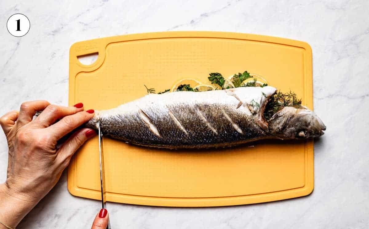 Cutting through the tail of a whole roasted branzino on a cutting board as the first step in deboning.