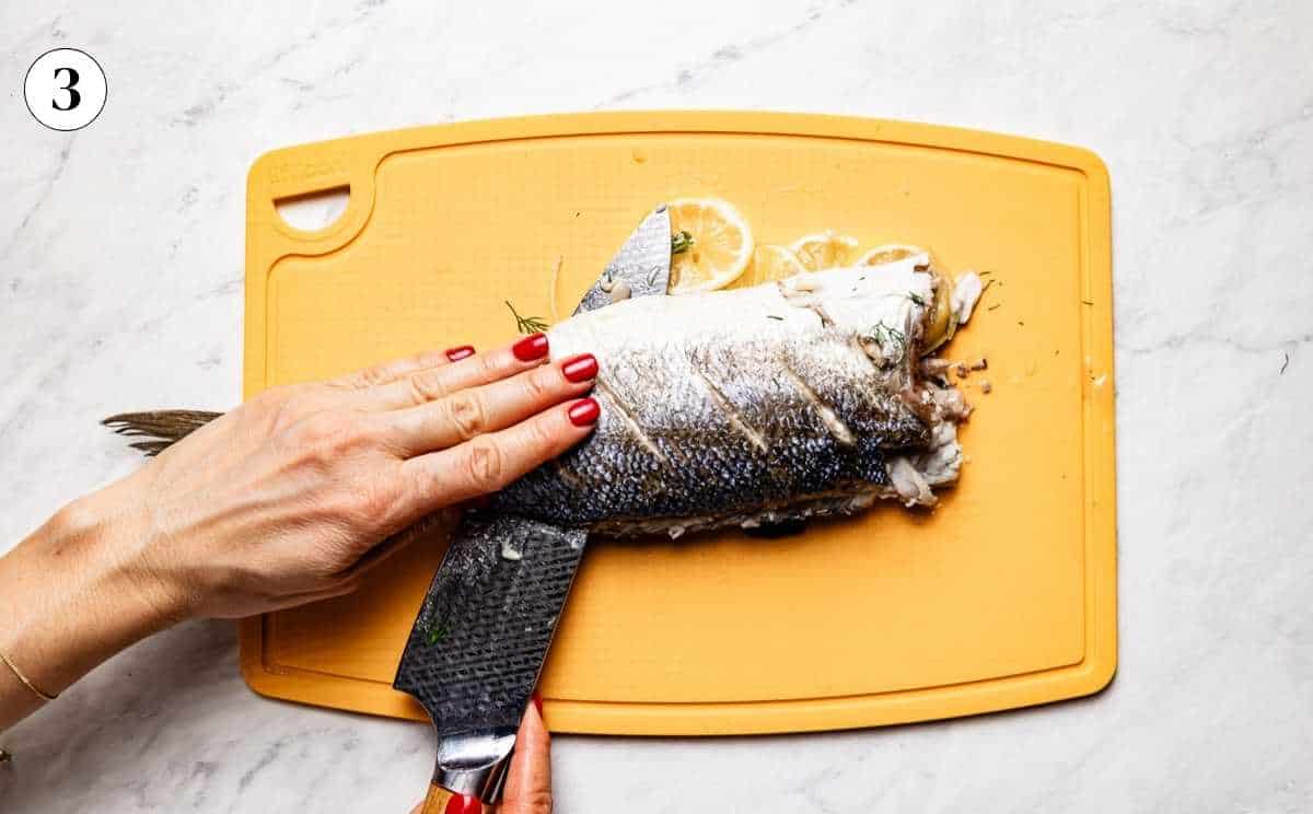 Sliding a knife parallel along the backbone of a roasted branzino to separate the top fillet.