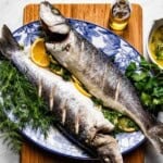 Two whole roasted branzino garnished with lemon and fresh herbs on a plate.