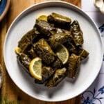 A white bowl of homemade dolmas stuffed with ground beef and rice, garnished with lemon slices, shot from overhead.