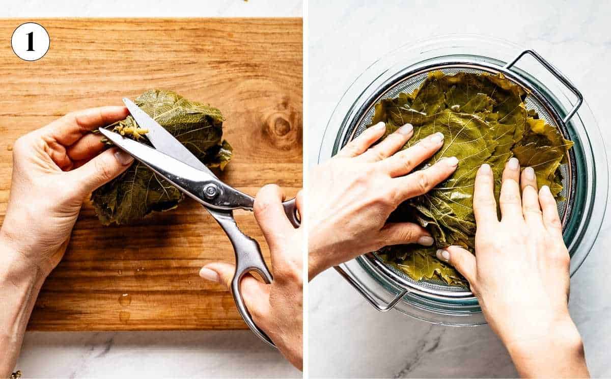 A woman is trimming the tough stem from a jarred grape leaf with scissors on a cutting board, and pressing rinsed grape leaves flat in a colander to drain.