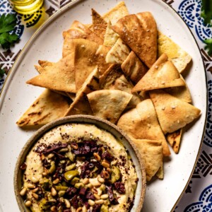 Homemade baked pita chips served with a bowl of hummus from the top view.
