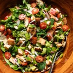 Overhead close-up of fattoush salad with crispy pita, halved cherry tomatoes, sliced radishes, and fresh herbs in a wooden bowl.