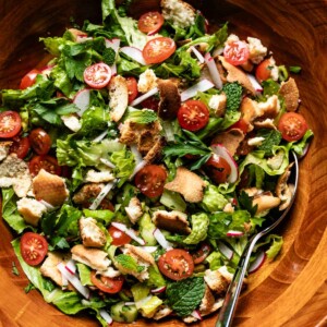 Overhead close-up of fattoush salad with crispy pita, halved cherry tomatoes, sliced radishes, and fresh herbs in a wooden bowl.
