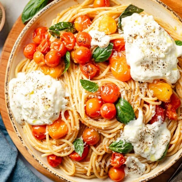 A large bowl with burst cherry tomato and burrata pasta garnished with basil.
