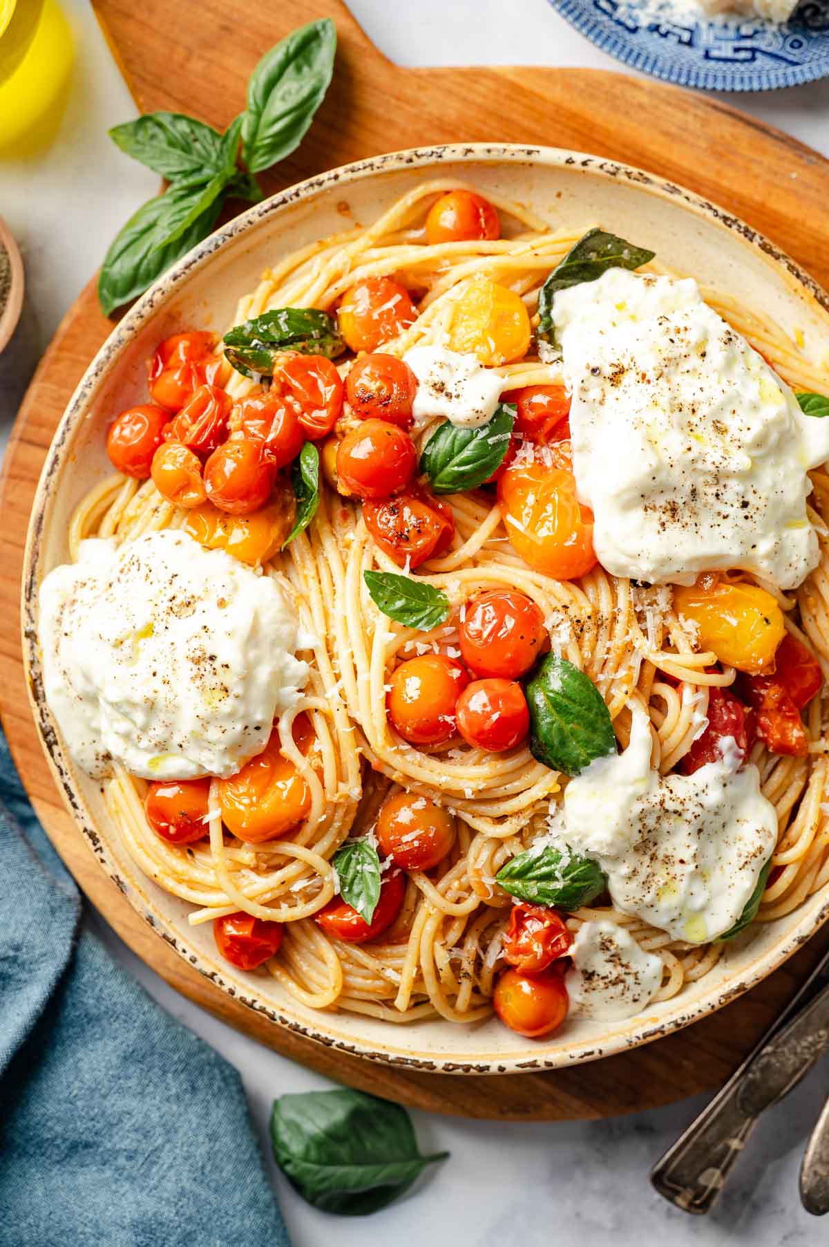 A large bowl with burst cherry tomato and burrata pasta garnished with basil.