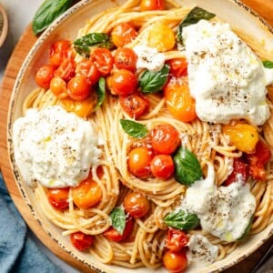A bowl of creamy burrata pasta with burst cherry tomatoes and fresh basil in a yellow bowl from the top view.