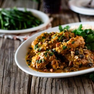 A plate of curried chicken breasts garnished with parsley from the front view.