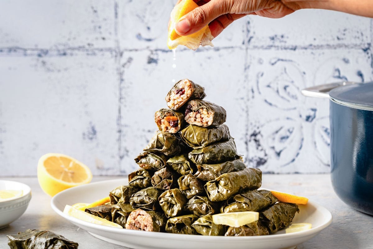 Person squeezing lemon juice over vegetarian stuffed grape leaves (dolmas) on a plate.