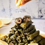 Person squeezing lemon juice on dolmas on a plate with the name of the recipe on the image.