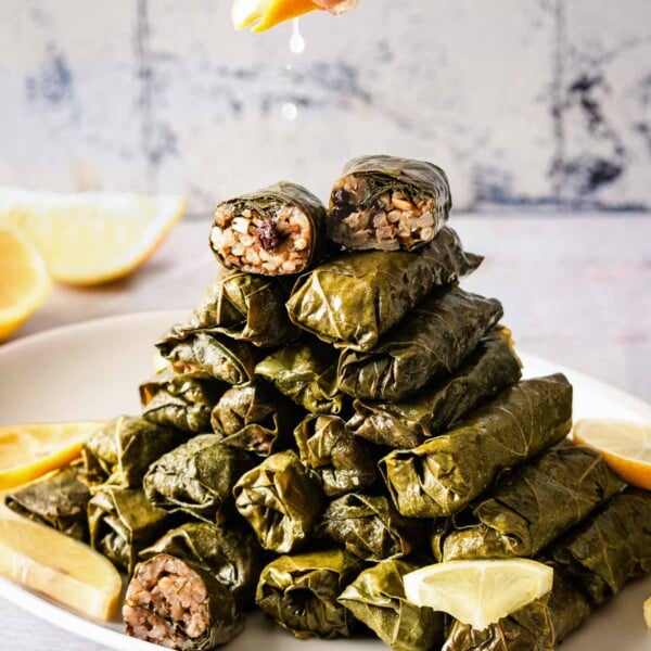 A person is squeezing lemon juice over vegetarian stuffed grape leaves arranged on a plate from the front view.