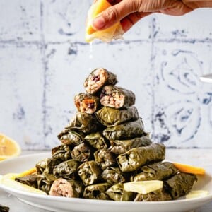 A person is squeezing lemon juice over stuffed grape leaves piled on a plate like a tower.