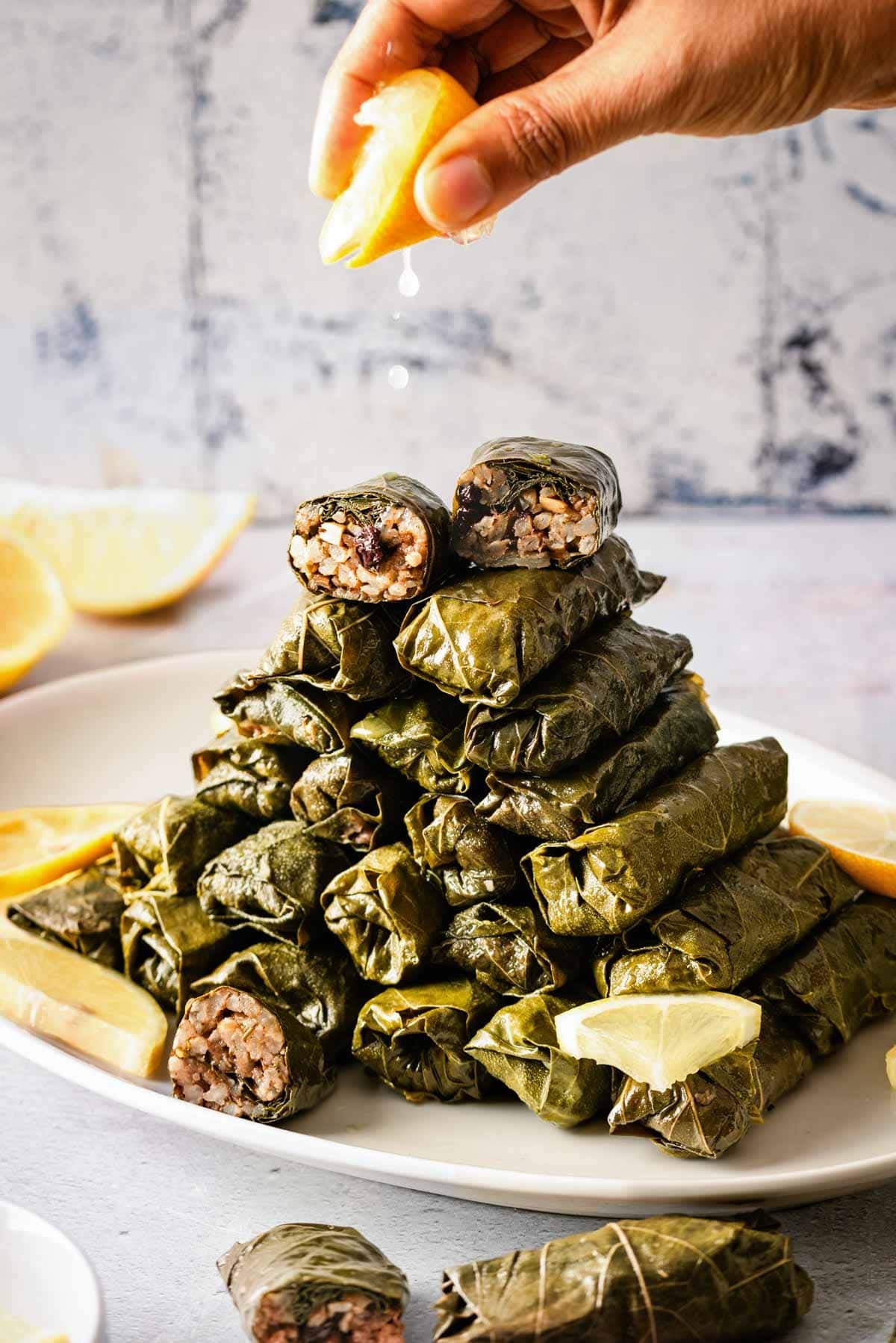 A person is squeezing lemon juice over vegetarian stuffed grape leaves arranged on a plate from the front view.