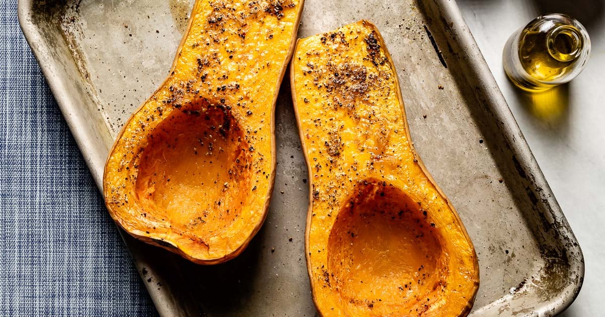 Roasted butternut squash halves, cut side up, on a sheet pan with a small bottle of olive oil.
