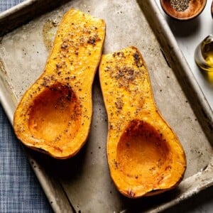 Freshly roasted butternut squash halves tender and slightly caramelized on a sheet pan from the top view.